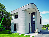 Zweistöckiges, graues Haus mit runden Ecken und Wulstwänden, das im 3-D-Betondruck gefertigt wurde