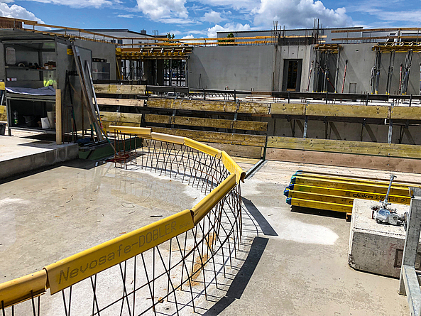 Detailaufnahme auf einer Baustelle, die im Vordergrund eine runde Anschlussbewehrung zeigt, auf die gelbe Schutzprofile gesteckt wurden.