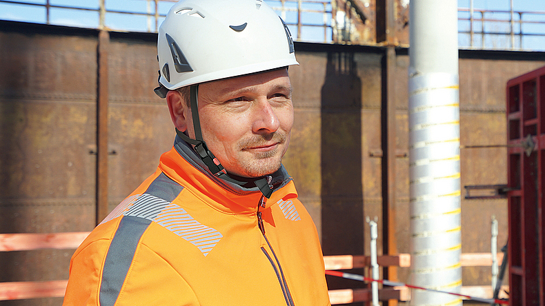 Porträt von Carsten Hofmann mit Helm und Arbeitskleidung auf der Baustelle.
