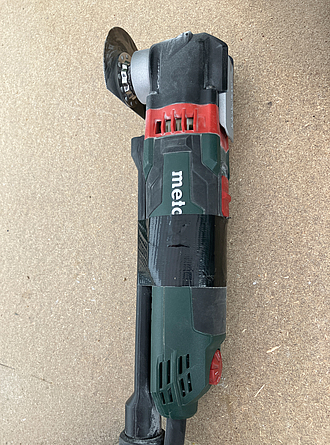 Multitool mit Sägeblatt und einem schwarzem Schlauchaufsatz liegt auf einem Boden.