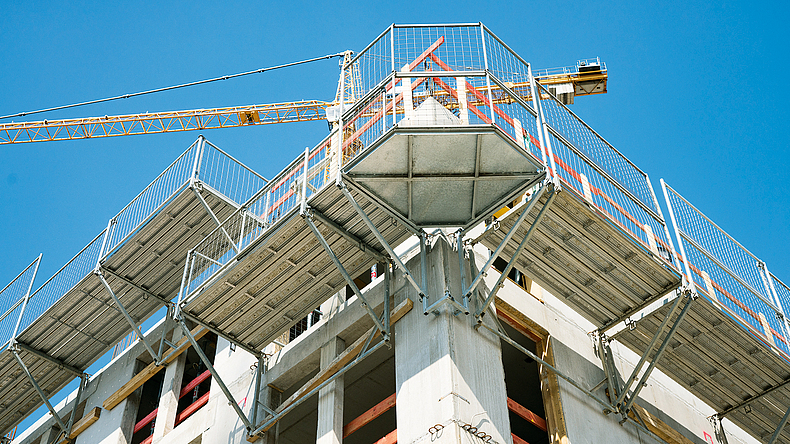 Blick von unten auf ein Konsolgerüst über Eck an einem Rohbau.