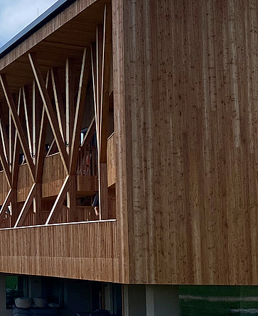 Ein Gebäude mitten in den Alpen. Das Erdgeschoss ist aus Beton gebaut. Der obere Teil ist eine komplexe Holzkonstruktion.