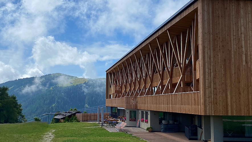 Ein Gebäude mitten in den Alpen. Das Erdgeschoss ist aus Beton gebaut. Der obere Teil ist eine komplexe Holzkonstruktion.