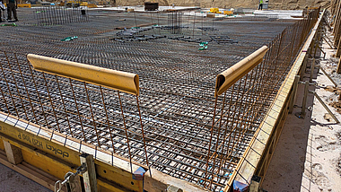Gitterförmig verlegte Bewehrungsstäbe einer Betondecke. Am Schalungsrand sind gelbe Schutzprofile angebracht, die hervorstehende Bewehrung sichern.