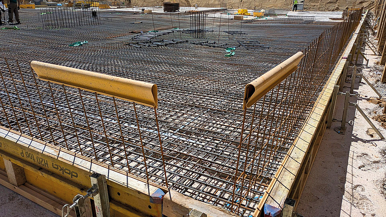 Gitterförmig verlegte Bewehrungsstäbe einer Betondecke. Am Schalungsrand sind gelbe Schutzprofile angebracht, die hervorstehende Bewehrung sichern.