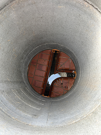 Blick von oben in einen runden Betonschacht mit drei gebogenen Rohröffnungen am Boden und ohne Steigeisen.