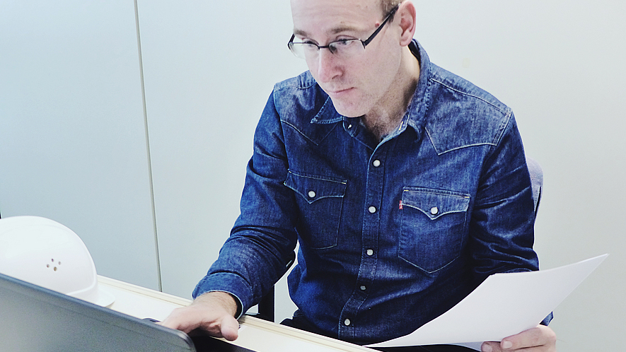 Ein Mann sitzt am Laptop mit Unterlagen in der Hand.