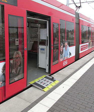 Eine gelb-graue Rampe überdeckt den Spalt zwischen Straßenbahn und Haltesteig. 