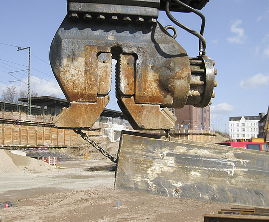 Spundwandgreifer und mit Kette gesicherter Stahlträger auf einer Baustelle
