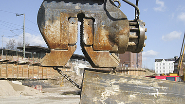 Spundwandgreifer und mit Kette gesicherter Stahlträger auf einer Baustelle