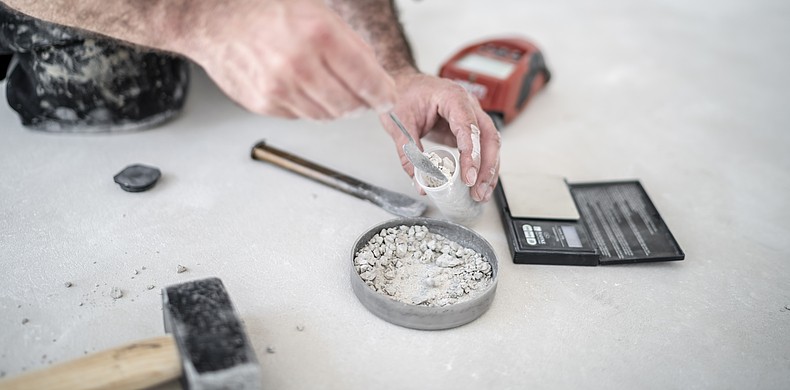 Estrichleger nimmt eine Probe des frisch zerkleinerten Estrichs, um den Feuchtigkeitsgehalt zu messen.