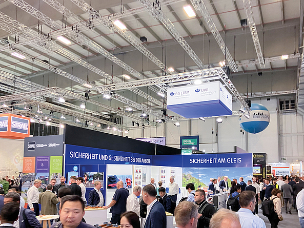 Besucherinnen und Besucher auf einer Fachmesse vor einem Messestand mit der Aufschrift „Sicherheit am Gleis“.