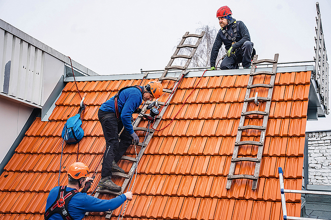 Trainer mit Dachdeckern bei der Unterweisung für Persönliche Schutzausrüstung gegen Absturz. 