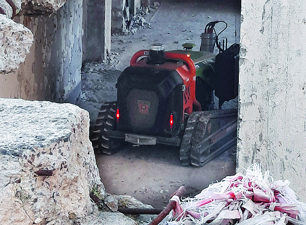 ein unbemanntes Kettenraupen-Fahrzeug fährt durch ein abgebrochenes Gebäude, Spezialfahrzeuge für die INN-Technik ermitteln nicht nur an der Erdoberfläche Messwerte zur Kampfmittel-Beseitigung, sondern auch auf bewehrten Beton-Gründungssohlen, in Mauerwerk, durch Spundwände hindurch und in Gebäuden.