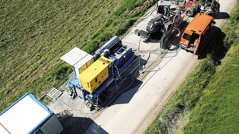 Mehrere Baumaschinen für das Spülbohrverfahren stehen auf einem Weg zwischen zwei grünen Feldern.