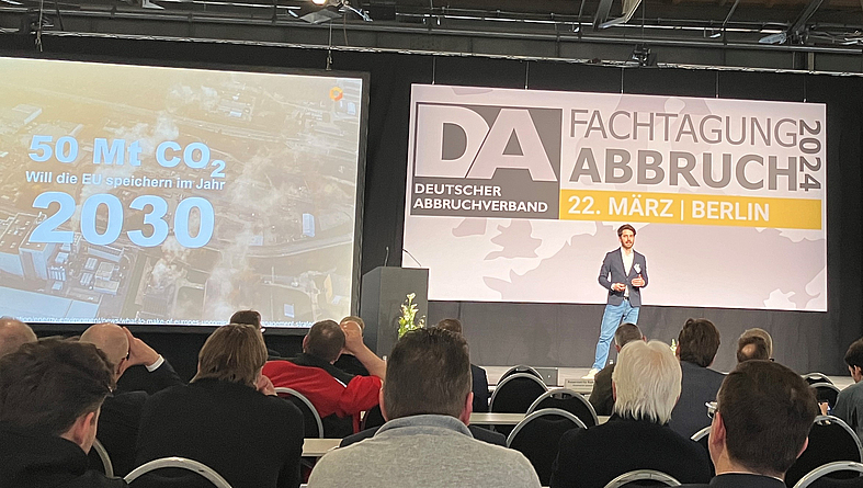 Vortrag von Valentin Gutknecht  Ein Mann spricht auf dem Podium zum Publikum.