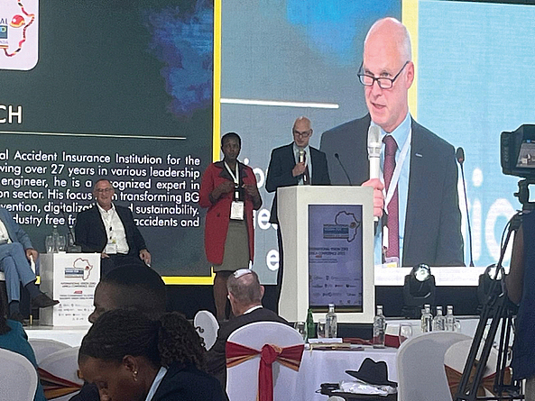 Ein Mann spricht am Rednerpult auf einer Konferenzbühne. Neben ihm steht eine Frau. Im Hintergrund ist eine große Leinwand mit seiner Projektion zu sehen.