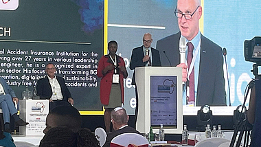 Ein Mann spricht am Rednerpult auf einer Konferenzbühne. Neben ihm steht eine Frau. Im Hintergrund ist eine große Leinwand mit seiner Projektion zu sehen.