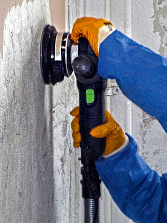 Der Putz von der Wand wird mit Hilfe eines Bearbeitungssystems mit Absaugung entfernt.