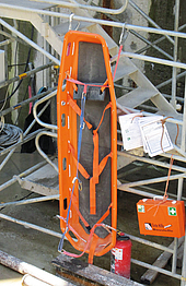 Eine orange Trage, die senkrecht an einem Treppenturm hängt. Dieser befindet sich in einem Baufeld.