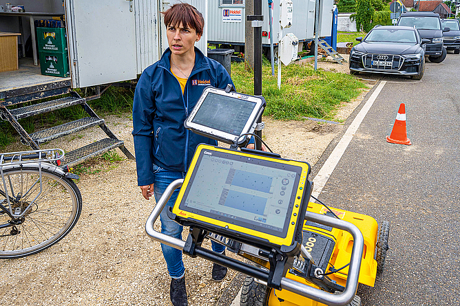 Die Fremdsparten werden mit dem Bodenradar geortet und in die digitale Planung übertragen. Betriebsbesichtigung auf einer Baustelle: Eine Frau neben einem Radargerät, auf dem zwei Tablets angebracht sind.