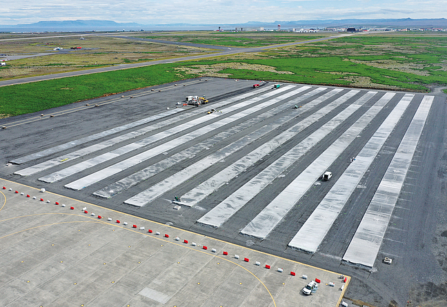 Luftaufnahme vom Vorfeld des Flughafens mit beeindruckenden Ausmaßen: Links hinten klein im Bild zu sehen, zieht der Gleitschalungsfertiger seine Bahnen. Von 31 geplanten Einzel-Betonbahnen sind 11 fertiggestellt. 