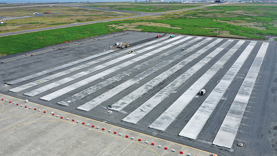 Luftaufnahme vom Vorfeld des Flughafens mit beeindruckenden Ausmaßen: Links hinten klein im Bild zu sehen, zieht der Gleitschalungsfertiger seine Bahnen. Von 31 geplanten Einzel-Betonbahnen sind 11 fertiggestellt. 