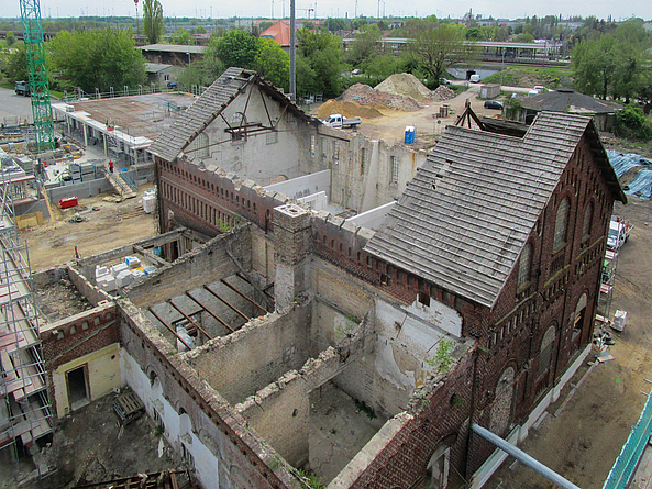 Teilweise abgerissenes Backsteingebäude auf einer Baustelle, mit freigelegten Innenräumen und umliegenden Bauarbeiten.
