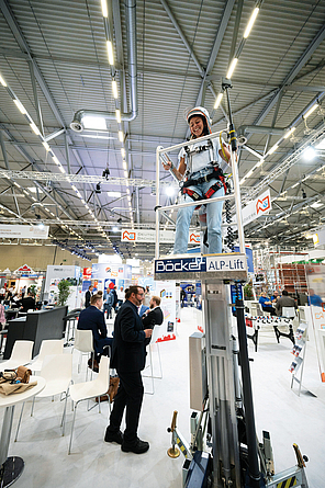 Impression vom Messestand, an dem gerade eine Frau mit PSA oben auf einer Hubarbeitsbühne steht.