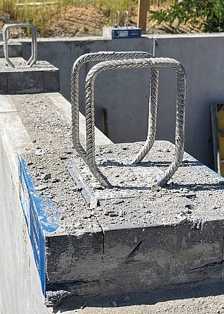 Betonbauteil mit herausragenden Bewehrungsbügeln auf einer Baustelle.