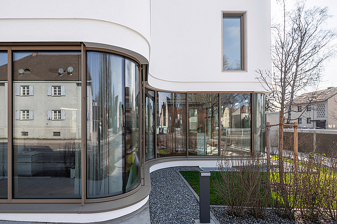 Detailaufnahme einer geschwungenen Außenwand mit Fensterfront.