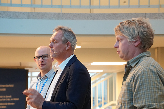 Stephan Thomas, Marco Einhaus und Harald Dippe auf dem 8. Fachkongress für Absturzsicherheit in der DASA Drei Männer stehen nebeneinander auf einer Bühne.