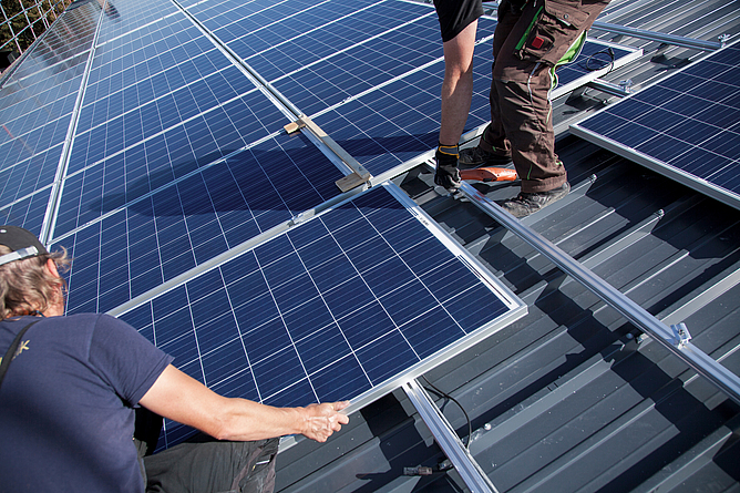 Die Montage von Photovoltaikanlagen ist mit Herausforderungen verbunden. Photovoltaikmodule werden von zwei Arbeitern auf einem Steildach installiert.