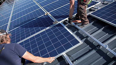 Photovoltaikmodule werden von zwei Arbeitern auf einem Steildach installiert.
