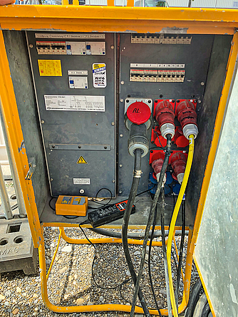 Baustromverteiler mit FI Blick auf einen geöffneten Baustromverteiler mit mehreren roten Steckern.