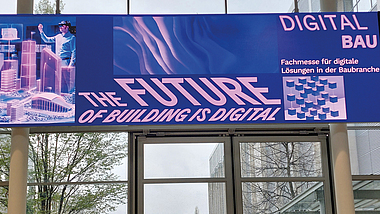Banner über einem Eingang mit der Aufschrift „THE FUTURE OF BUILDING IS DIGITAL“ und „DIGITAL BAU – Fachmesse für digitale Lösungen in der Baubranche“.