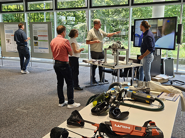 An einem Infostand mit PSA in einem Gebäude stehen Personen.