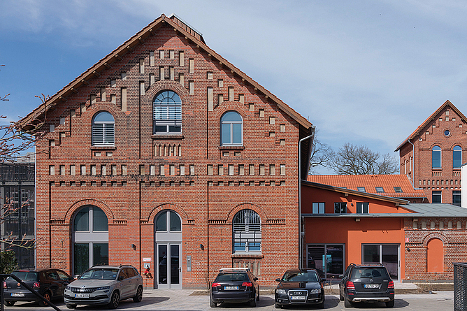 Saniertes Backsteingebäude mit symmetrischer Fassade und parkenden Autos davor.