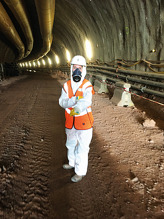 Ein Beschäftigter im Brandbergtunnel trägt persönliche Schutzausrüstung (Schutzanzug, Warnweste, Helm, Atemschutzmaske) wegen des asbesthaltigen Gesteins im Tunnel.