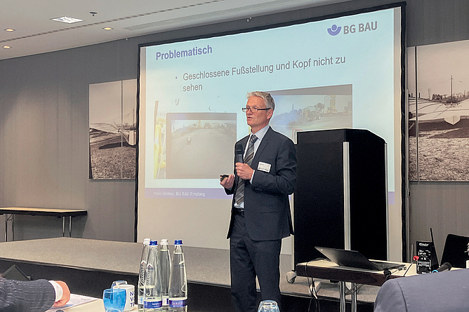 Ein Mann vor einer Präsentationswand hält einen Vortrag. 