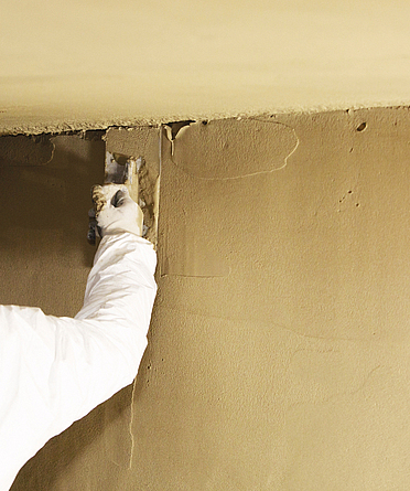 Ein Mann mit blauem Basecup glättet den soeben aufgespritzten Brandschutzputz.