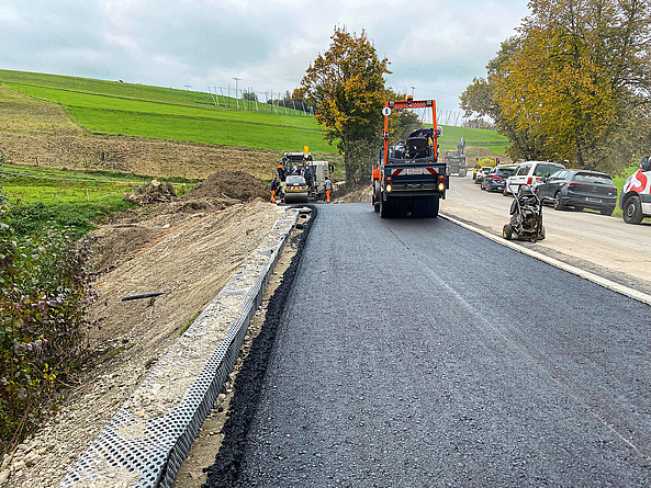 Eine Baumaschine fährt über eine frisch asphaltierte Straße.