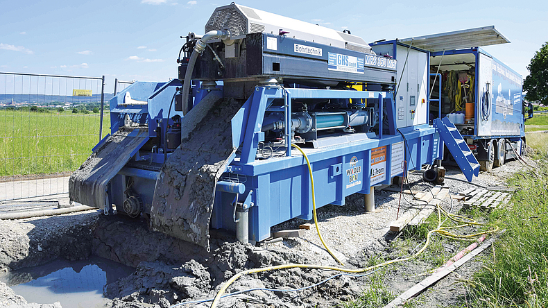 Aus einer großen Maschine läuft Spülmaterial in eine Grube auf dem Weg.