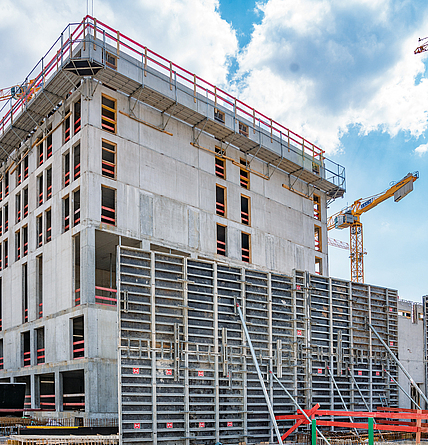 Eine Rahmenschalung steht vor einem mehrstöckigen Rohbau aus Beton.