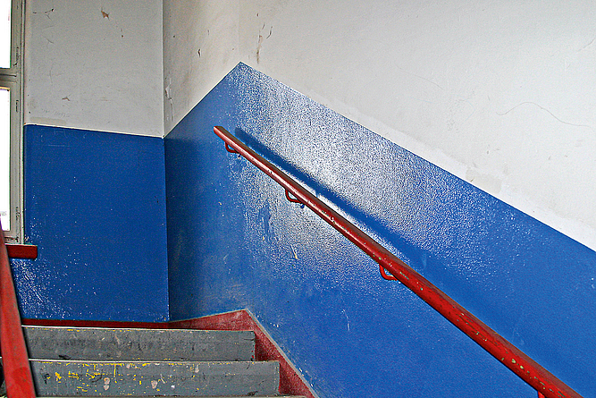 Wand eines Treppenhauses, die in Grau und leicht glänzendem Blau gestrichen ist.