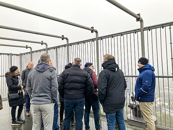 Gruppe von Menschen, die sich auf dem umzäunten Dach des Gasometers befindet und einer Person, die etwas erklärt, zuhört.