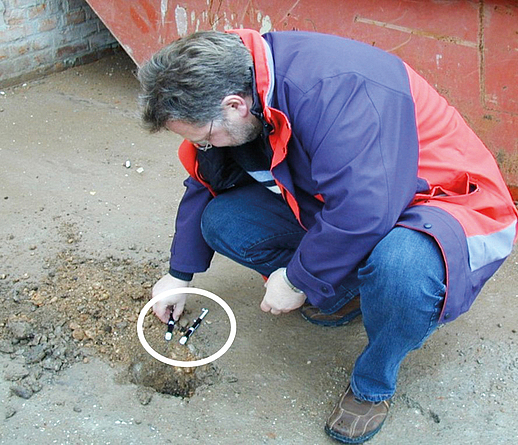 Eine Person kniet auf dem Boden mit einem spritzenförmigen Probenbecher. 