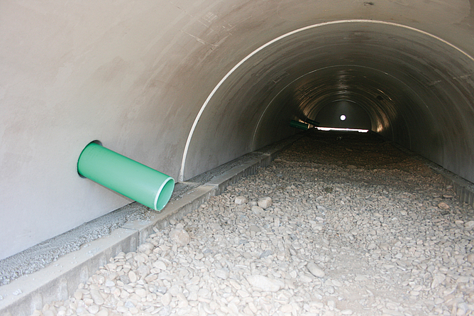 Innenansicht eines Sickertunnels aus Stahlbeton mit Kiesbett und seitlich eingeführtem Rohr.