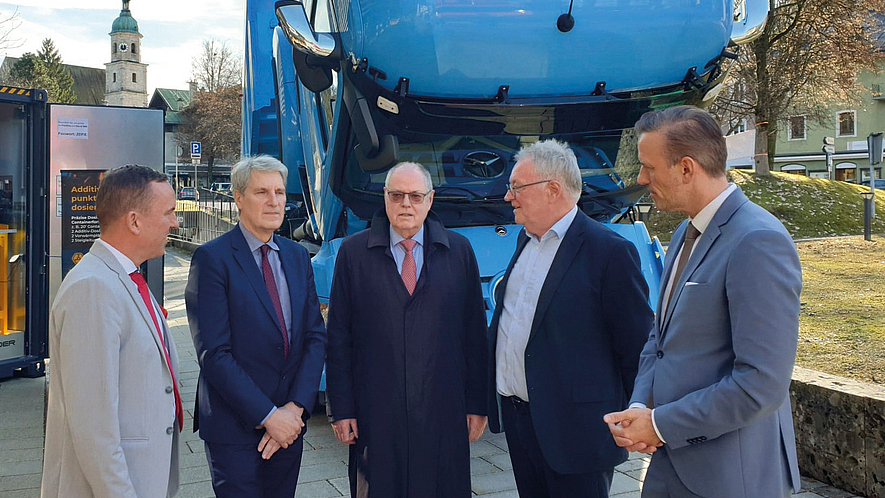 Fünf Männer in Anzügen stehen im Freien vor einem angehobenen blauen Lkw-Fahrerhaus; mittig Peer Steinbrück, umgeben von Vertretern des Deutschen Asphaltverbandes.