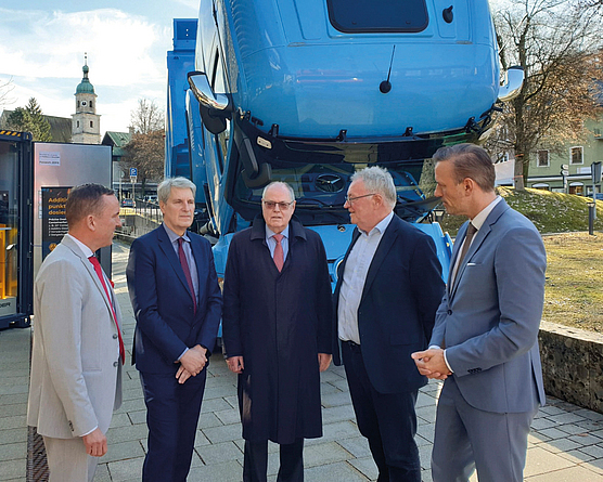 Fünf Männer in Anzügen stehen im Freien vor einem angehobenen blauen Lkw-Fahrerhaus; mittig Peer Steinbrück, umgeben von Vertretern des Deutschen Asphaltverbandes.